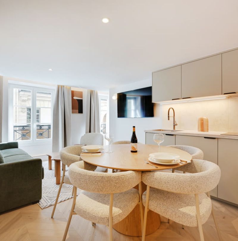 Coin repas avec table ronde en bois, chaises crème et canapé vert